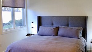 Ein Schlafzimmer mit einem großen Bett, einem Deckenventilator, einem Fenster mit Jalousien und einem Nachttisch mit Lampe.