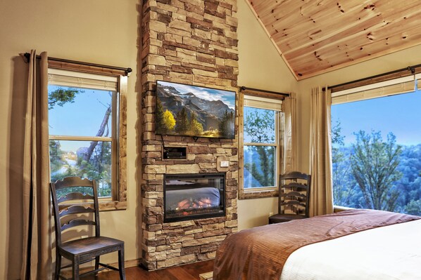 Una habitación con chimenea de piedra, una cama y ventanas amplias con vistas a la montaña.
