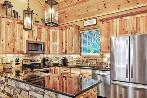 A kitchen with wooden cabinets, a stainless steel refrigerator, a built-in stove, and a stone backsplash.