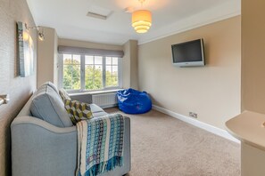 A room with a sofa, a blue bean bag, a television on the wall, and a window with a view of trees. - 3 Bed in Lynton (oc-keepba) (Ilkerton)