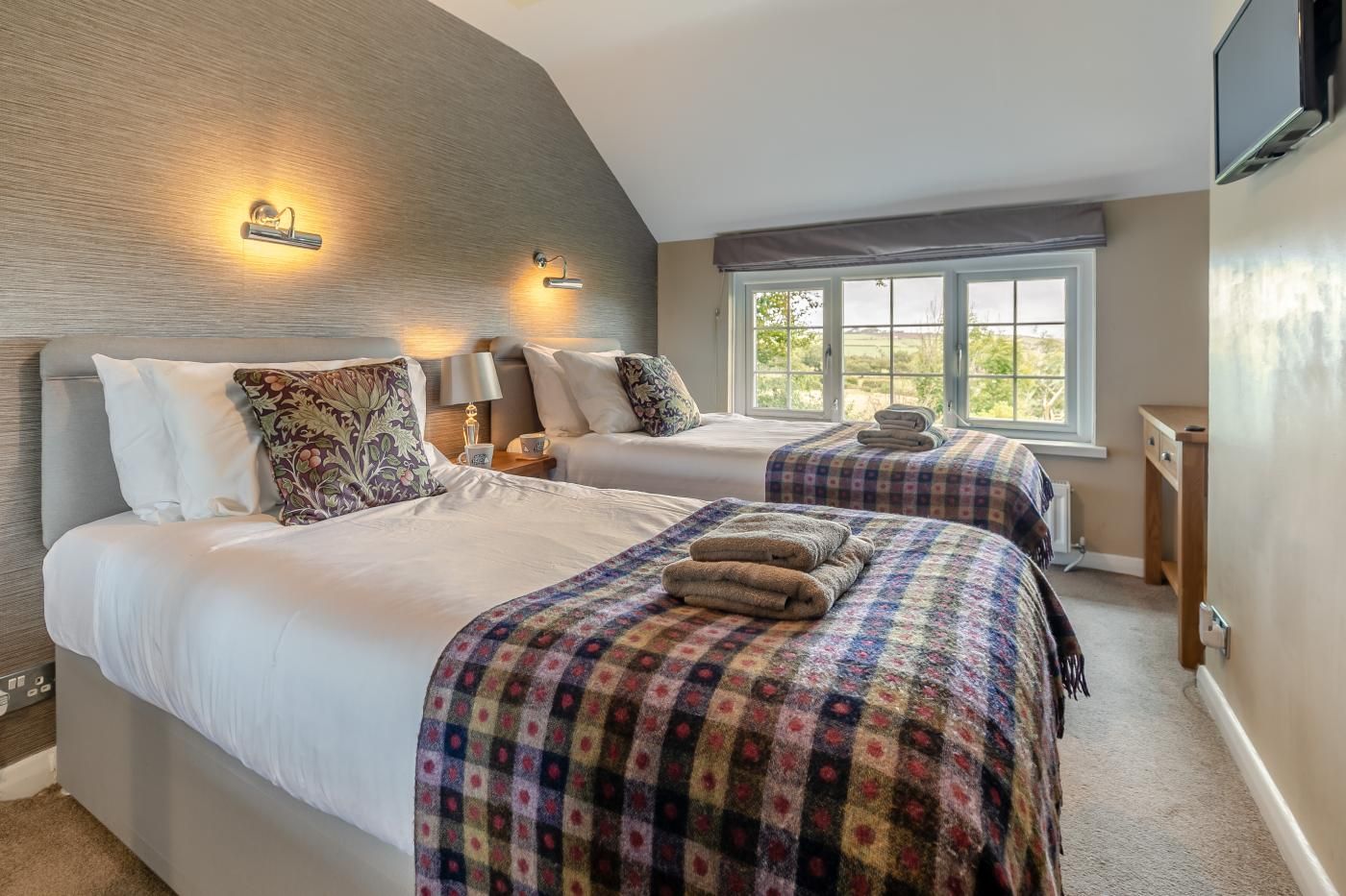 A bedroom with two beds, a window, and a television.