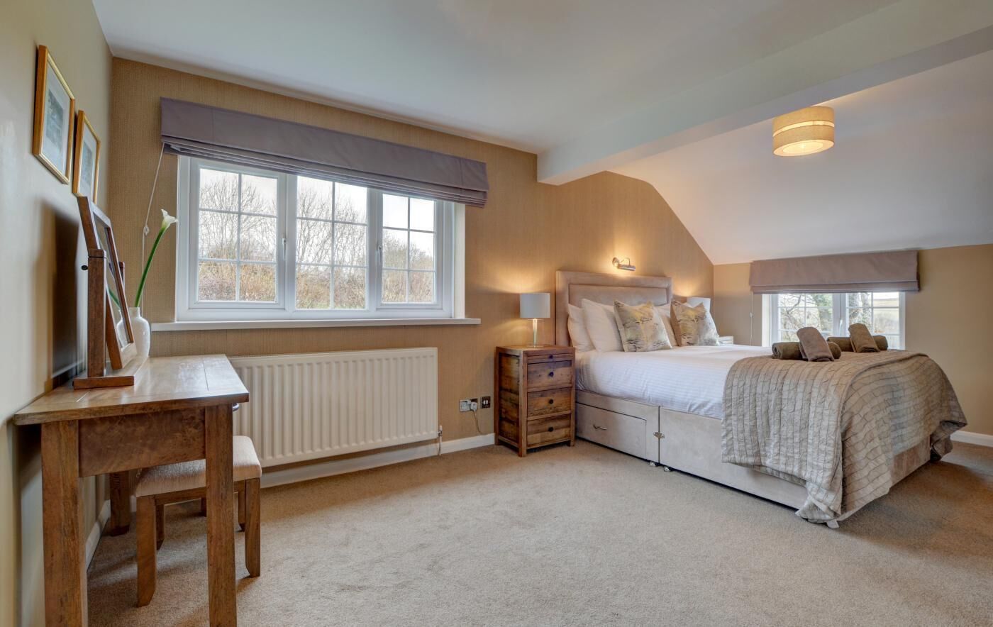 A bedroom with a bed, bedside table, lamp, radiator, and a window with blinds.