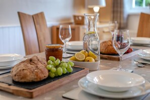 A breakfast setting with a loaf of bread, a bowl of grapes, lemons, a jar of jam, and a pitcher of water on a table. - 3 Bed in Lynton (oc-keepba) (Ilkerton)