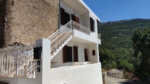 A two-story building with a white exterior, a balcony with a metal railing, and a staircase leading to the upper floor. - "Sa Dommu 'e su coro" apartment for 2. (Triei)