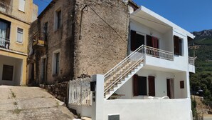 A two-story building with a white facade, a stone wall, and a staircase leading to the upper floor. - "Sa Dommu 'e su coro" apartment for 2. (Triei)