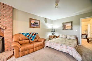 A bedroom with a brick fireplace, a leather sofa, a bed with a floral bedspread, a small table with a lamp, and a mirror on the wall. - Walkout Apartment w/ Mtn View on Cortez Ranch (Cortez)