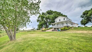 A large, two-story house with a porch and a flag, surrounded by a well-maintained lawn and trees. - Walkout Apartment w/ Mtn View on Cortez Ranch (Cortez)