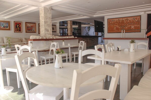 Un restaurante con mesas y sillas blancas, una zona de bar y obras de arte en las paredes.