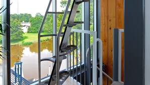 Un interior moderno con una escalera de metal que conduce a un balcón con vistas a una masa de agua.