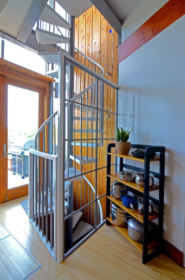 Un escalier en colimaçon avec des rampes en métal, un mur en bois et un coin cuisine avec des étagères et des ustensiles de cuisine.