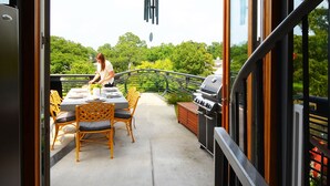 Puerta abierta que da a un patio al aire libre con una mesa, sillas y una parrilla.