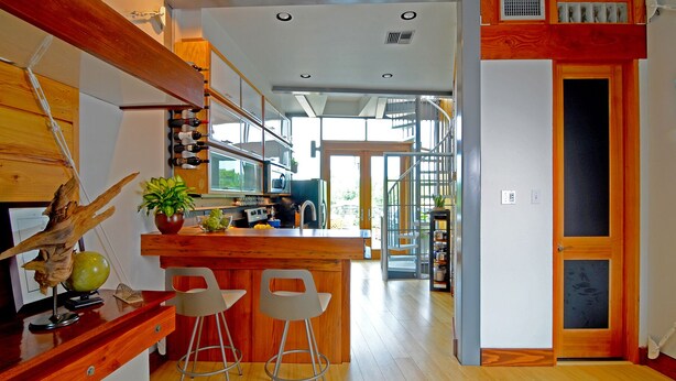 Una cocina moderna con barra de madera, dos taburetes y un ventanal grande.