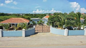 Área residencial murada com entrada pavimentada, parede azul e casa com telhado de telhas vermelhas.