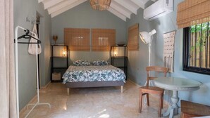 Quarto com cama, mesas de cabeceira, uma cadeira, uma mesa e janela com persianas.