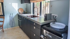 Uma cozinha moderna com armários escuros, uma pia de aço inoxidável, uma máquina de café e uma lava-louças embutida.