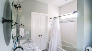 Un baño con lavamanos de mármol, una puerta blanca, una bañera y una cortina de ducha.