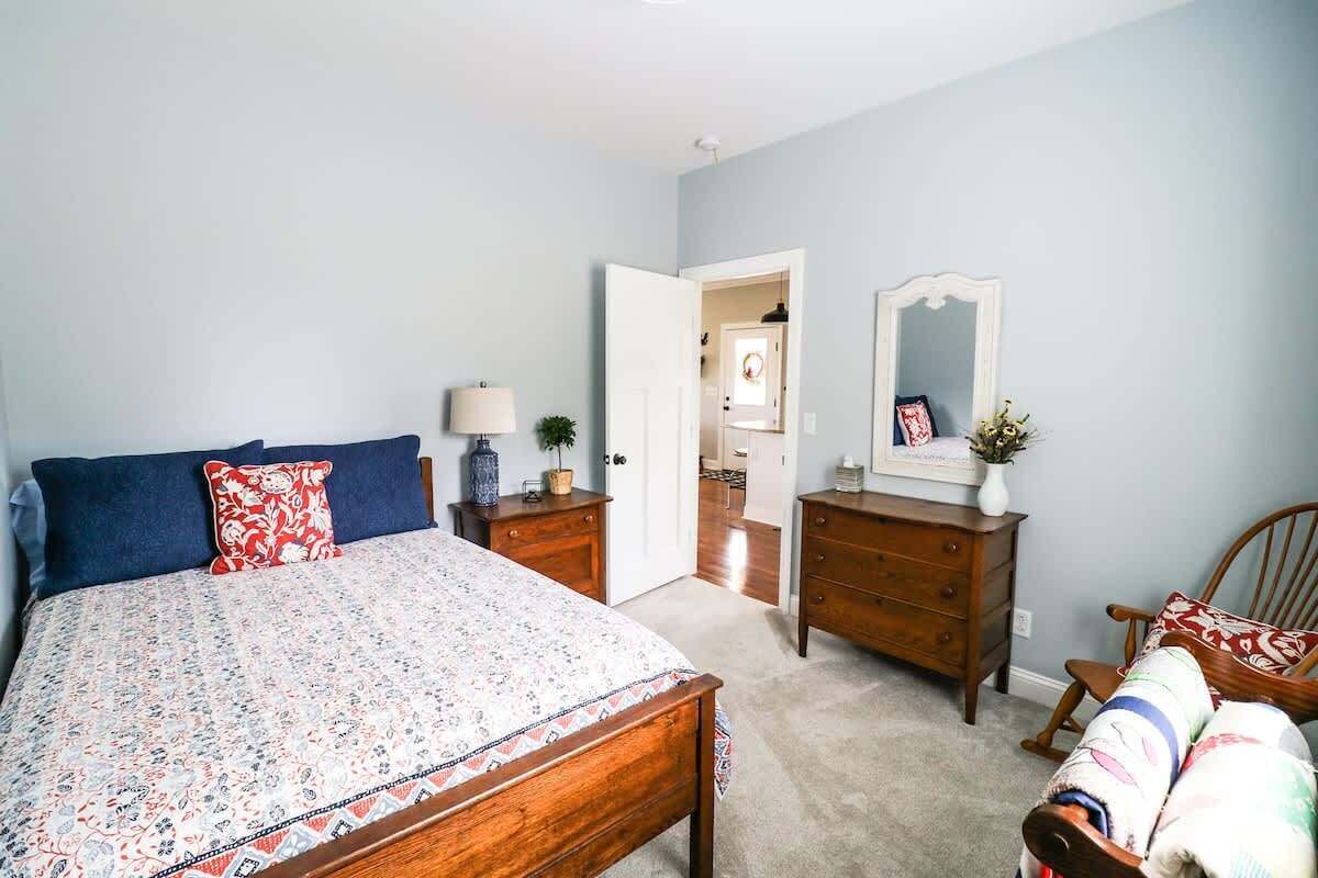Um quarto com cama, penteadeira, cadeira e porta que dá para outro espaço.