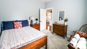 Un dormitorio con cama, cómoda, silla y puerta que da a otra habitación.
