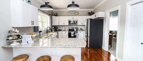 Una cocina moderna con armarios blancos, encimera de granito y tres taburetes de madera.