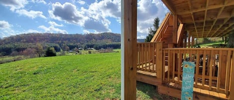 Une cabane en bois dotée d’un balcon donnant sur un champ verdoyant et des collines.