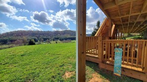 Een houten chalet met balkon, met uitzicht op een groen veld en heuvels.