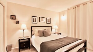 A neatly arranged bedroom with a bed, two bedside tables, and a nightstand. There are framed pictures on the wall, a lamp on each bedside table, and a window with curtains. - Spacious and Beautiful, Walk to ski, Wi-fi, Parking (Park City)