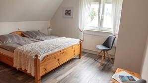 Makuuhuoneessa on puinen sänky, tuoli, pieni pöytä ja ikkuna, jossa on verhot.