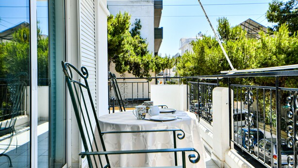 A balcony with a table set for two, chairs, and a view of parked cars and trees. - Alcyone, Comfortable Home Close To Athens Airport (Artemis)