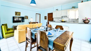 A dining area with a table set for four, a television, and a sofa in a room with light blue walls. - Alcyone, Comfortable Home Close To Athens Airport (Artemis)