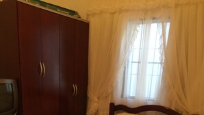 Une chambre à coucher avec un lit, une armoire, une télévision et une fenêtre avec des rideaux.