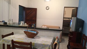 Un coin repas avec une table dressée pour deux personnes, un panier en osier posé sur la table et un téléviseur en arrière-plan.