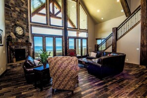 A spacious living room with a fireplace, leather furniture, and large windows offering a view of the outdoors. - Hidden Chateau | Idaho's Largest Vacation Rental | 13BR Sleeps 52 | Private Beach, Pools & Theater (Fish Haven)