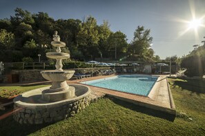 Una piscina amb una font de pedra, envoltada per una zona verda i arbres.
