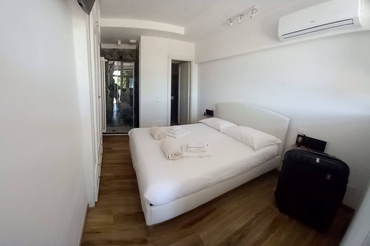 A modern hotel room with a large bed, a suitcase, and a view of the outside.