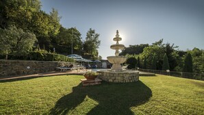 A stone fountain with a tiered design, surrounded by a well-maintained lawn and a stone wall. - Rocca Palazzaccio (Impruneta)