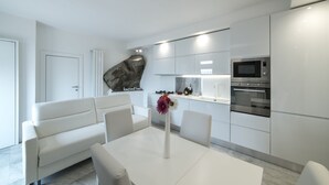A modern kitchen with white cabinetry, a built-in microwave, and an oven. There is a white dining table with a vase of flowers. - Rocca Palazzaccio (Impruneta)