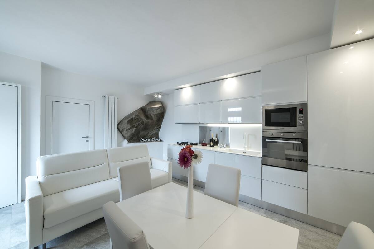 A modern kitchen with white cabinetry, a built-in microwave, and an oven. There is a white dining table with a vase of flowers.