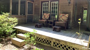 A wooden porch with two chairs and a table, a wooden fence, and a sign that reads "Farmhouse".