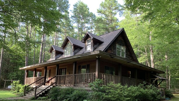 A wooden cabin with a porch, a staircase, and a view of the surrounding forest.