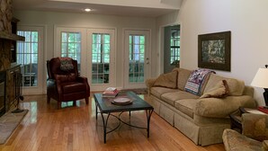 A spacious living room with a high ceiling, a fireplace, a leather armchair, a sofa, and a coffee table.