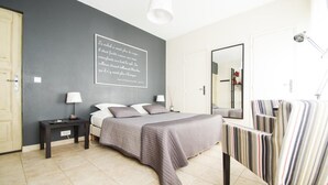 A bedroom with a bed, bedside tables, a mirror, and a striped chair. - Comfort double beige room (Cabriès)