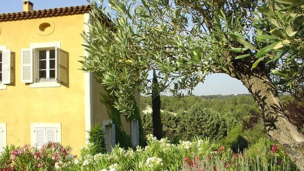 A yellow building with white shutters, surrounded by a garden with various flowers and a large tree. - Comfort double beige room (Cabriès)