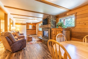 Relax by the fireplace in this inviting cabin, featuring a comfortable chair, dining table, and large window with a view.