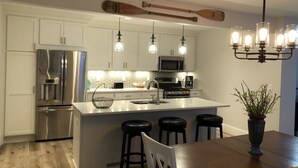 A modern kitchen with white cabinets, stainless steel appliances, a large island with stools, and a unique wooden paddle hanging above.