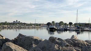 A marina with boats docked, a rocky shoreline, and buildings in the background.