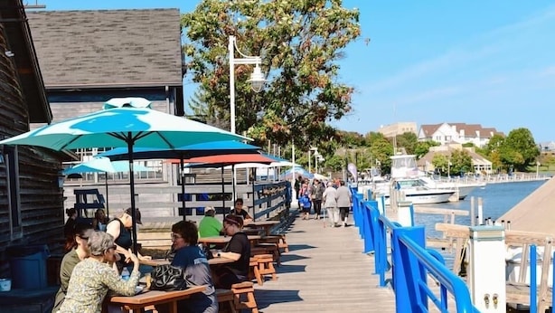 A wooden pier with benches and umbrellas, overlooking a body of water with boats.