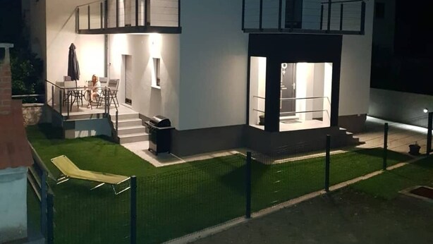 Une maison moderne à deux étages, dotée d ’un balcon, d’un petit porche fermé et d’un espace extérieur bien éclairé, aménagé pour se détendre.