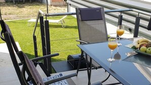 Une terrasse extérieure avec une table dressée pour deux personnes, agrémentée d’un verre de jus d’orange et d’une assiette de fruits.