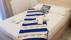 Un lit bien fait, recouvert d’une couverture à rayures, un oreiller orné d’un motif noué et, au mur, une photographie représentant un paysage côtier.
