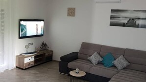 Un salon moderne avec un téléviseur à écran plat, un canapé, une petite table d’appoint et une horloge murale.